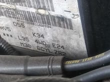 Located to the right of the heater core hoses, directly behind the distributor. Notice the zr2 at the bottom right of the sticker...