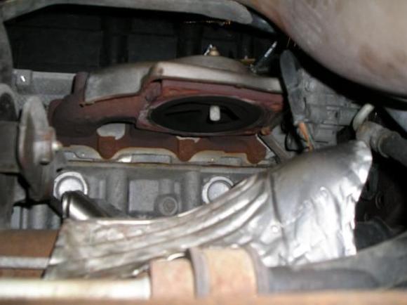Heres a picture of the rear exhaust manifold after unbolting the catalytic converter and laying it aside.  It wont come out.  Just set it on the crossmember to give yourself room to extract the Y-pipe.  Notice the heat shield on top of the manifold.  Its held in place with the same four bolts and nuts that hold the cat underneath, which means that when you re-assemble the cat to the manifold, you have to put the four bolts up through the new gasket, the manifold and the heat shield before you put on a nut.  Its a little tricky but the bolts are not evenly spaced around the cat so it can be assembled only in the proper orientation.  Use anti-seize on all the bolts and nuts when you re-assemble so the next guy has an easier time of it.  When you put it back together, remember to insert the Y-pipe over the crossmember before bolting up the cat.  Connect the Y-pipe loosely at all connections before tightening any of them. To finish the job, replace the structural brace, re-connect the O2 Sensors, replace the splash shield and pat yourself on the back.