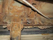 Front of cab bottom showing brake cable at top and part of running board bolts.  There is a hole in the the cab body into the rocker panel area. The stuff hanging down appears to be an earlier rocker panel repair. I haven't taken off the running boards yet, but some of the rockers seem to be OK, other part not good at all.