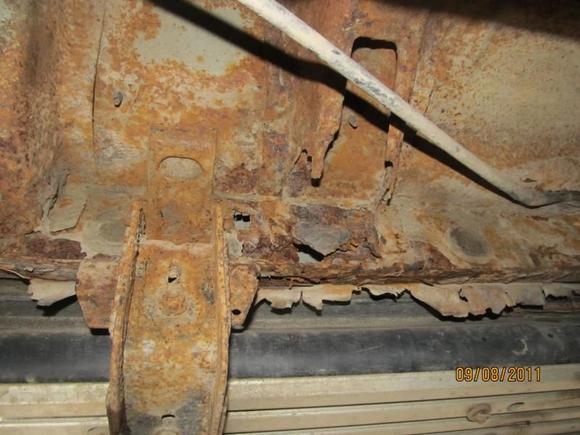 Front of cab bottom showing brake cable at top and part of running board bolts.  There is a hole in the the cab body into the rocker panel area. The stuff hanging down appears to be an earlier rocker panel repair. I haven't taken off the running boards yet, but some of the rockers seem to be OK, other part not good at all.