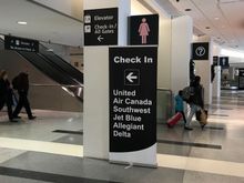 Signage right inside door from rental car shuttle near carousel #6 directing passengers to elevator for check-in for listed airlines. 