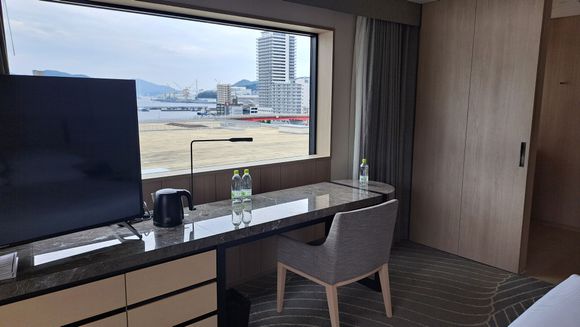 TV and desk with bathroom to right. Facing the bay and the conference centre roof. Fridge to the left