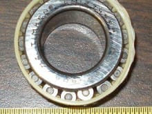 Inner side of OEM outer wheel bearing after cleaning.  The whitish material in a hard plastic that serves as a cage for the roller.  Timken LM12749PP.  11 years old.  The irregular looking material on the outer circumference appears to be a manufacturing defect.  No abnormal wear seen elsewhere on the bearing.