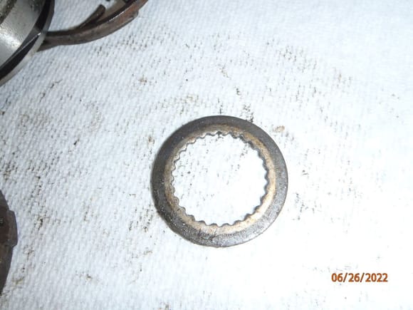 this washer is held in place by the smaller snap ring that rides in a groove on the axle stub shaft.  it can be removed when the snap ring is removed, but it is easier to get to once the brake assembly is removed